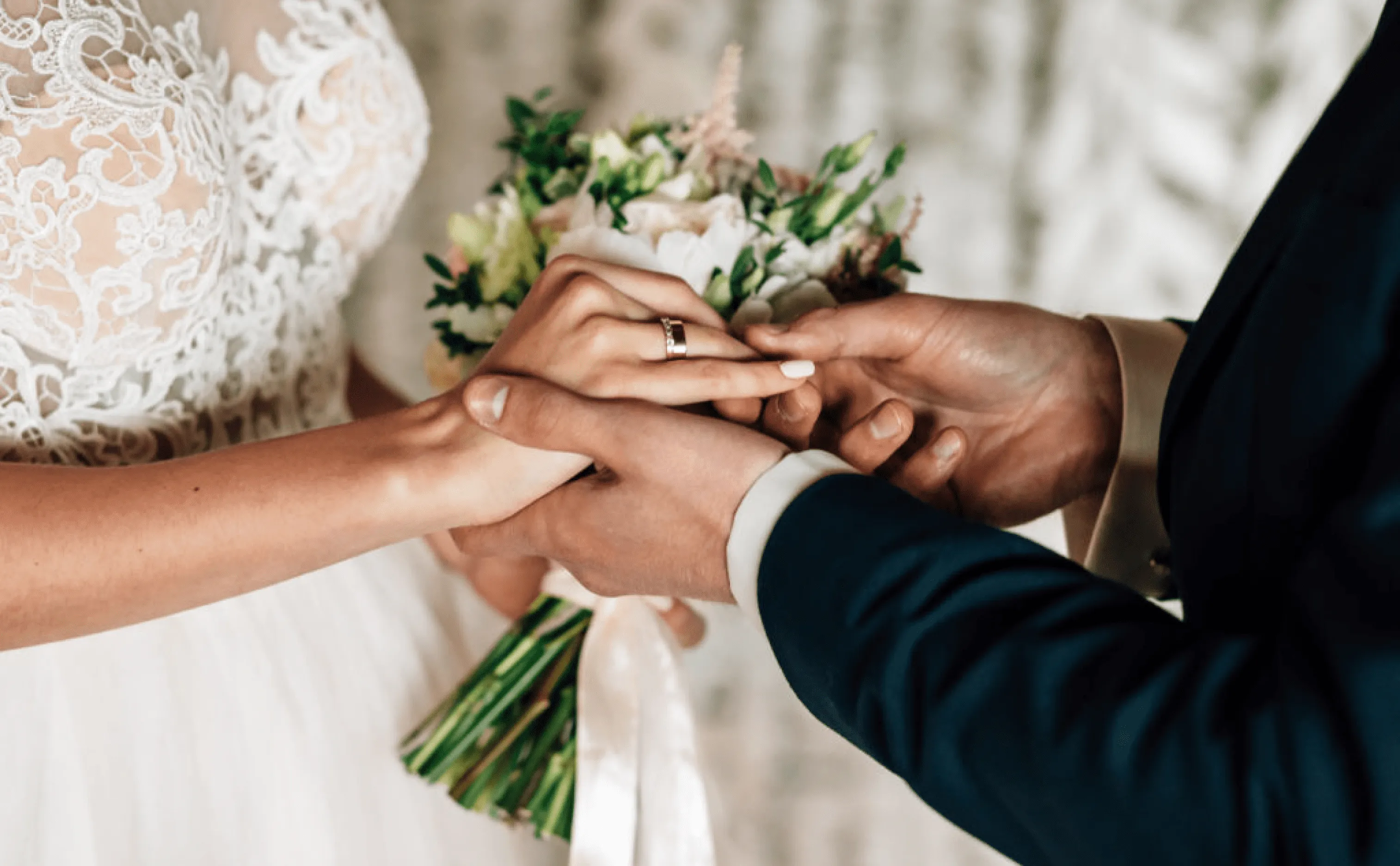 Les mains de deux mariés avec un bouquet de fleur en arrière plan