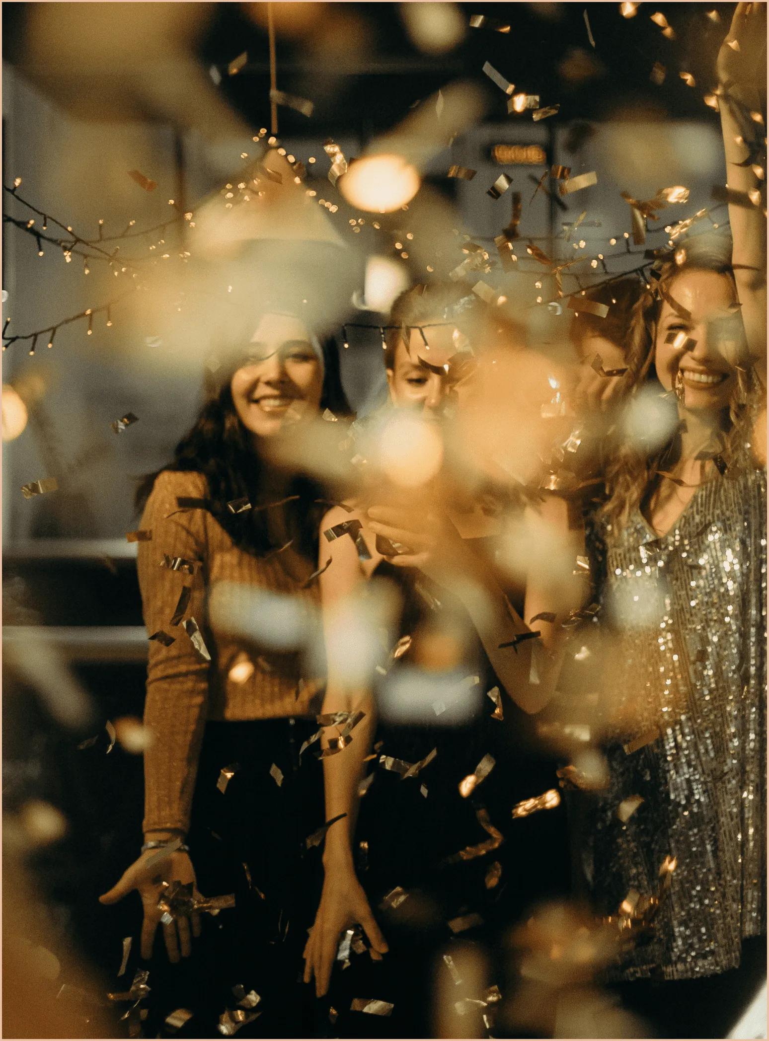 Trois femmes au milieu de confettis qui tombent. Les confettis sont de couleur dorée.